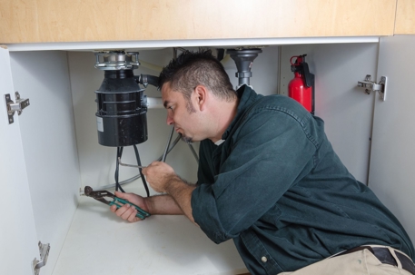 plumber under a sink with a flashlight
